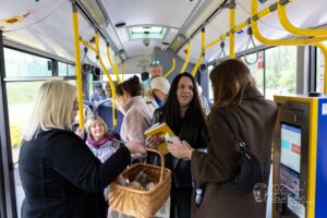 Wnętrze autobusu komunikacji miejskiej. Kobiety i mężczyźni rozdają pasażerom książki i ciastka pieguski.