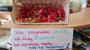 Koszyk z cukierkami oraz napis na kartce: "Kto przyniesie laurkę i złoży życzenia lub wypożyczy książkę... może się poczęstować