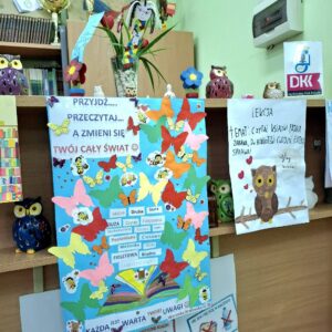 Plakat w kolorowe motyle i hasło zachęcające do czytania