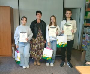3 młode osoby trzymają dyplomy i torby z nagrodami. 