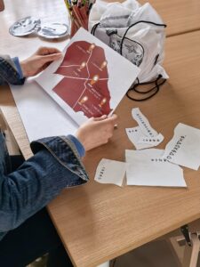 Osoba trzyma w rękach mapkę. Obok na stole leżą kartki z wydrukowanymi znakami.
