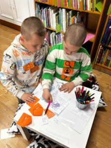 Dwóch chłopców wykonuje wspólnie zadanie przy stoliku w bibliotece. 