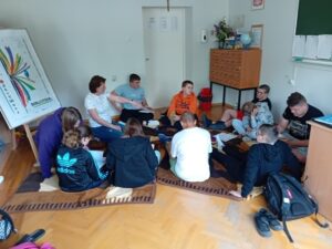 Grupa dziesięciorga nastolatków siedzi na podłodze. przeglądają ksiażki i dyskutują.