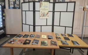 stół z projektami okładek książek, w tle plakat Tygodnia Bibliotek
